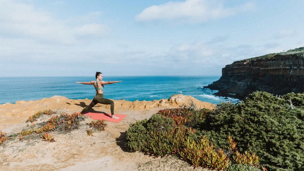 Woman doing yoga pose on cliff overlooking ocean